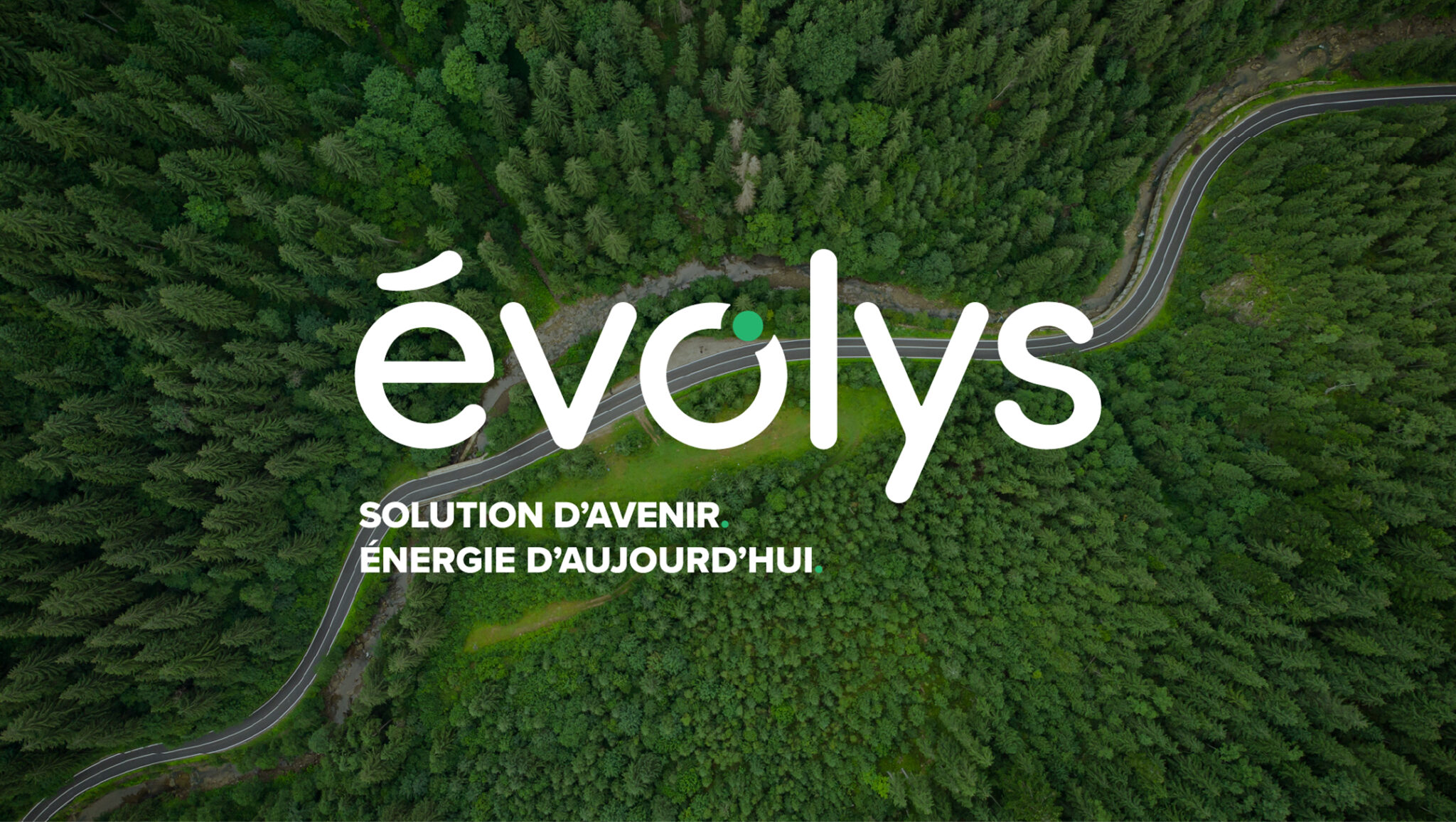 Une route sinueuse traverse une forêt verdoyante et dense. Sur l'image, on peut lire en lettres blanches : « évolys » et, en dessous, « Solution d'avenir, énergie d'aujourd'hui ».