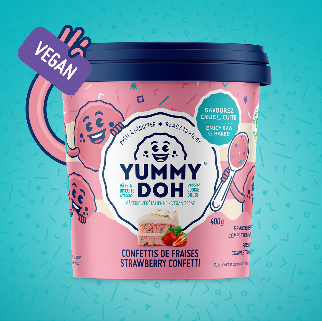 Un pot bleu de pâte à cookies végétalienne à la fraise « Yummy Doh », orné de visages souriants de personnages de dessins animés. L'étiquette indique « À déguster crue ou cuite au four » et « Friandise végétalienne », et représente une part de gâteau à la fraise parsemé de confettis.