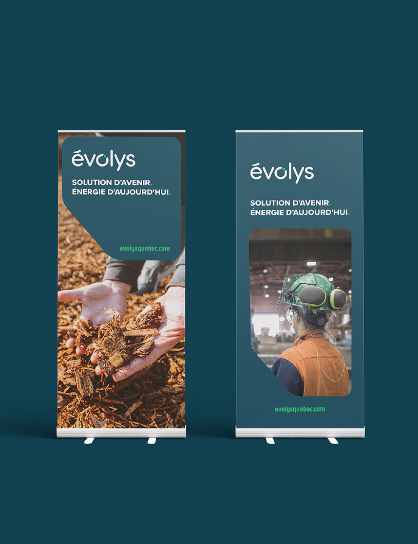 Deux bannières sur pied arborent le logo d’évolys. L’une montre un gros plan de mains tenant des copeaux de bois, tandis que l’autre représente une personne en équipement de sécurité sur un site industriel. Le texte indique : « Solution d’avenir. Énergie d’aujourd’hui. ».