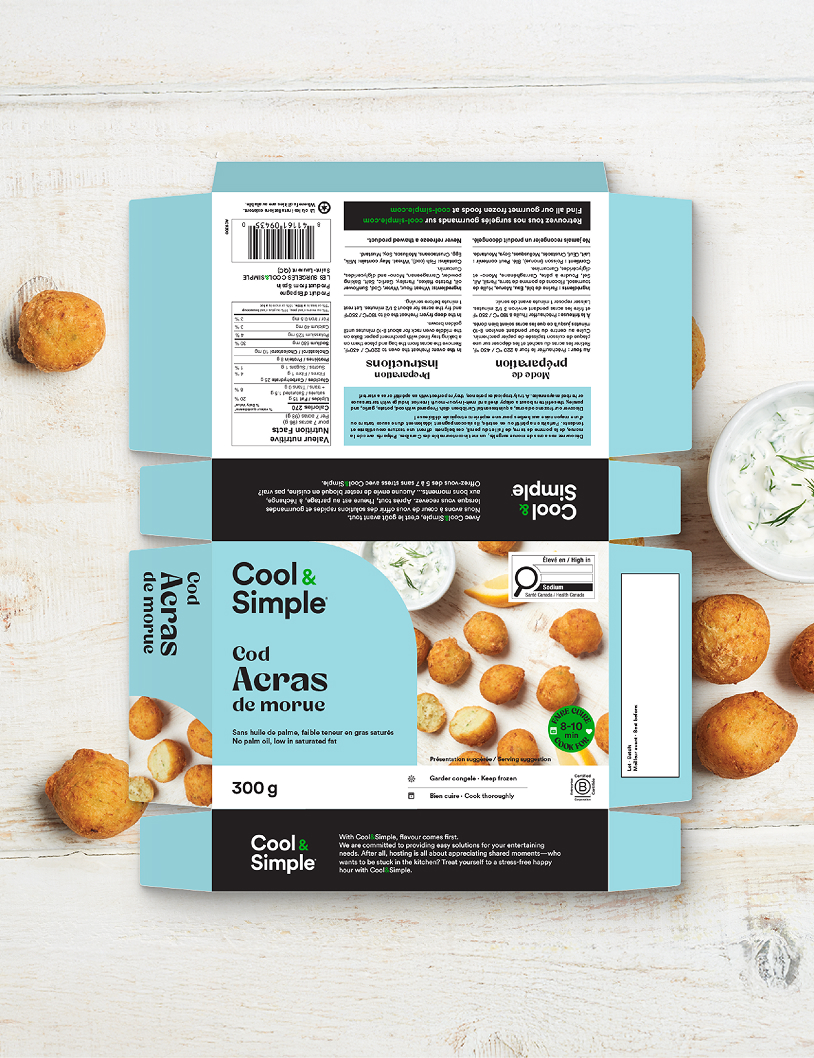 Photo « flat lay » de l'emballage des « Acras de morue Cool & Simple », montrant des beignets de morue dorés disposés sur un fond en bois blanc, accompagnés d'un bol de sauce et des informations sur le produit en anglais et en français sur une boîte bleue et noire.