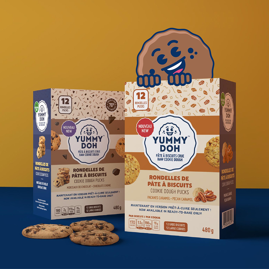 Deux boîtes de pastilles de pâte à cookies crue « Yummy Doh » sont disposées sur un fond bleu, avec des cookies devant. Un cookie de dessin animé souriant sort de l'une des boîtes. L'arrière-plan est divisé en deux parties, l'une jaune et l'autre bleue.