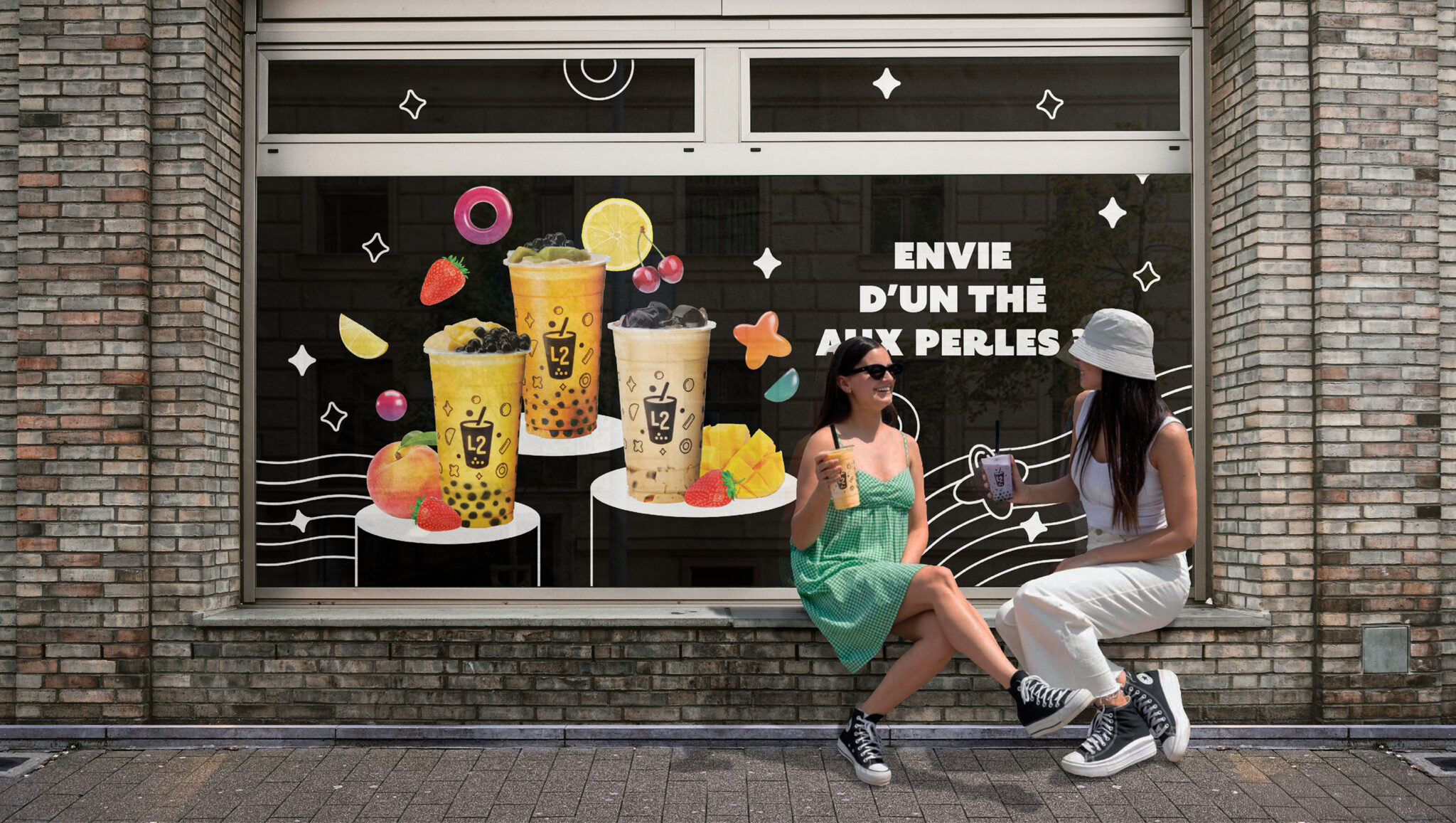 Deux femmes sont assises sur le trottoir devant la vitrine d'un magasin décorée d'illustrations colorées représentant le thé aux perles L2 Bubble Tea et de motifs de fruits. Le texte sur la vitrine indique « ENVIE D'UN THÉ AUX PERLES ». Les deux femmes sourient et tiennent chacune une boisson au thé aux perles.