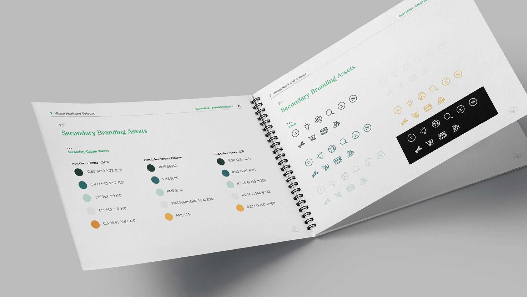 Un livret de charte graphique à reliure spirale, ouvert sur des pages présentant les palettes de couleurs secondaires ainsi qu’une variété d’icônes secondaires de la marque, dans différents styles et couleurs, sur un fond gris clair.