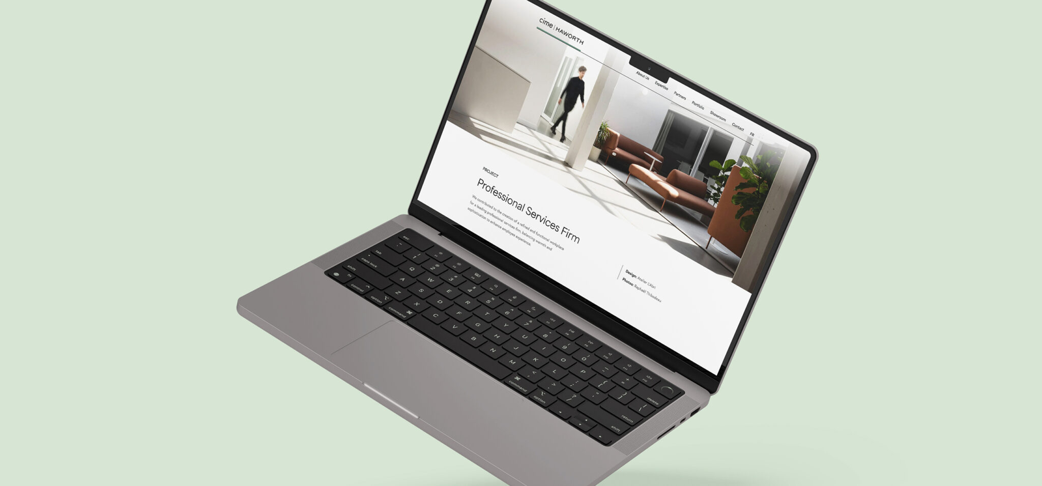 On voit un ordinateur portable gris sur un fond vert clair, affichant un site web au design moderne et minimaliste sur lequel apparaît une personne entrant dans une pièce lumineuse agrémentée de plantes d'intérieur et de mobilier contemporain.