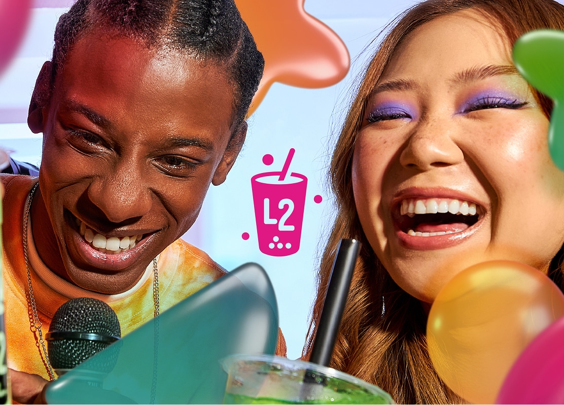 Deux jeunes qui sourient et rient, entourés de ballons colorés et d'une boisson au premier plan. L'un tient un micro ; l'autre porte un maquillage violet vif autour des yeux. Au centre se trouve l'icône d'un gobelet rose de thé aux perles portant la mention « L2 ».