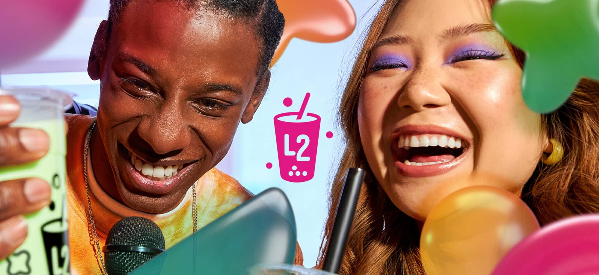 Deux amis souriants tenant chacun une boisson « L2 Bubble Tea », entourés de ballons colorés, avec un « L2 » rose et un motif représentant du bubble tea au centre. L'arrière-plan est lumineux et festif.