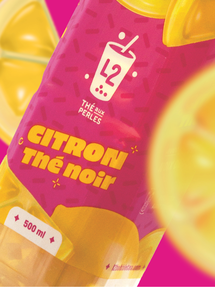 Gros plan sur une étiquette de boisson aux couleurs vives, rose et jaune, portant la mention « CITRON Thé noir », avec l'illustration d'un citron, le logo « L2 » et la mention « THÉ aux PERLES ». La contenance de la bouteille est indiquée comme étant de 500 ml.