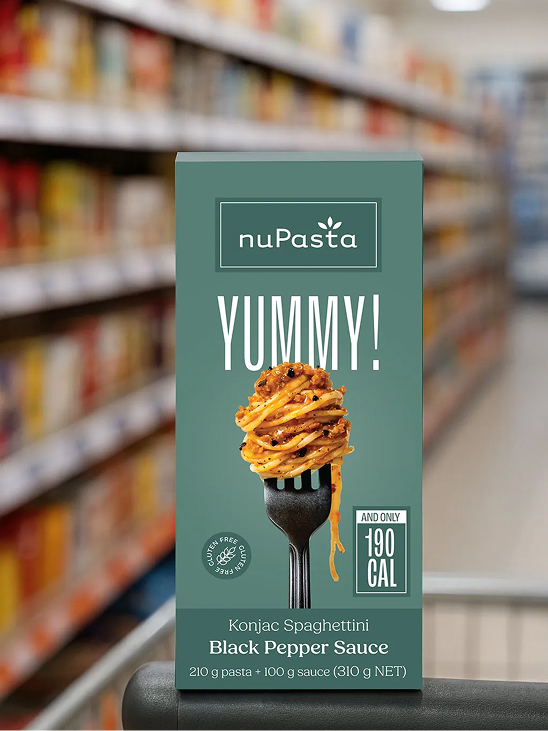 Une boîte de « nuPasta Konjac Spaghettini à la sauce au poivre noir » est exposée dans l'allée d'un supermarché ; elle présente une image de pâtes enroulées autour d'une fourchette, le mot « YUMMY ! » en gros caractères, ainsi qu'une étiquette indiquant 190 calories par portion.