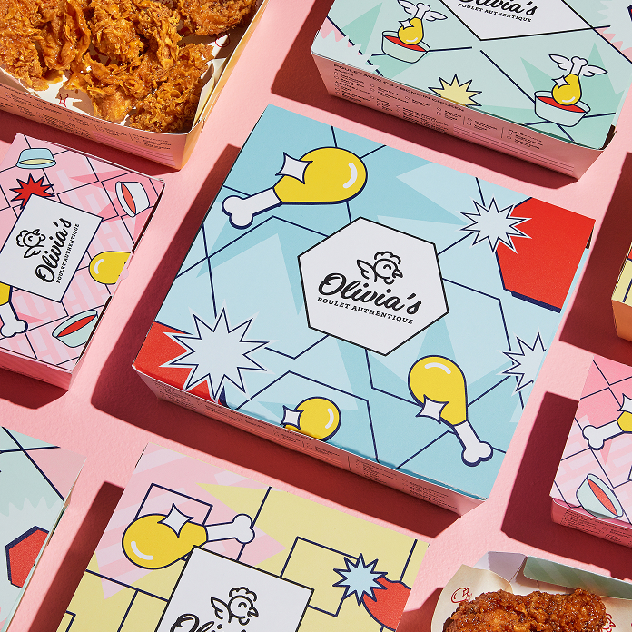 Les boîtes de poulet « Colorful Olivia », ornées de motifs ludiques représentant des pilons et des étoiles, sont disposées sur un fond rose ; certaines sont ouvertes, dévoilant un poulet authentique, doré et croustillant à l'intérieur.