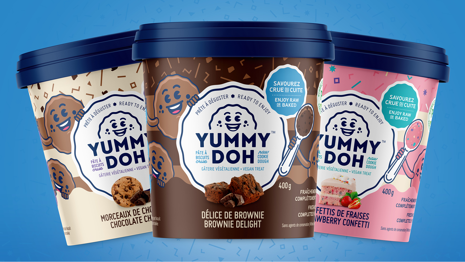 On voit ici trois pots colorés de pâte à cookies végane « Yummy Doh », aux saveurs « Chocolate Chunk », « Brownie Delight » et « Strawberry Confetti », chacun orné d'une mascotte souriante en forme de cookie et doté d'un couvercle bleu sur fond bleu.