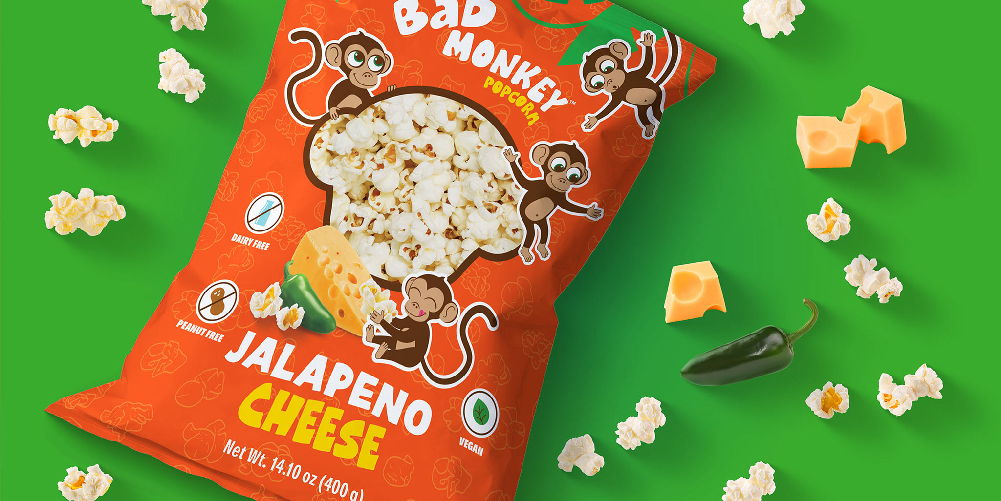 Un sachet de pop-corn « Bab Monkey Jalapeno Cheese » entouré de pop-corn en vrac, de cubes de fromage et d'un piment jalapeño sur fond vert.