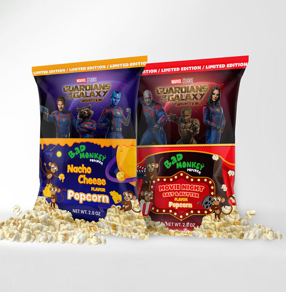 Deux sachets de pop-corn « Bad Monkey » à l'effigie des « Gardiens de la Galaxie », l'un à la saveur « Nacho Cheese » et l'autre à la saveur « Movie Night Salt & Butter », posés au milieu d'un tas de pop-corn.
